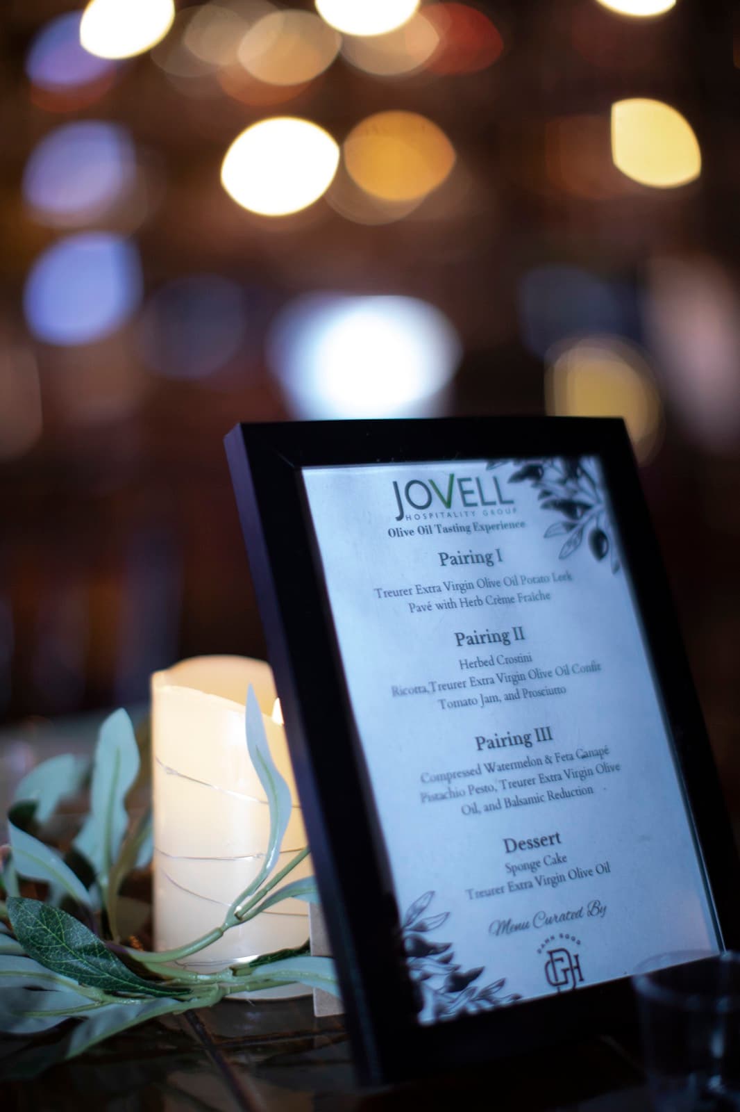 Olive oil tasting menu framed beside a candle and olive greenery