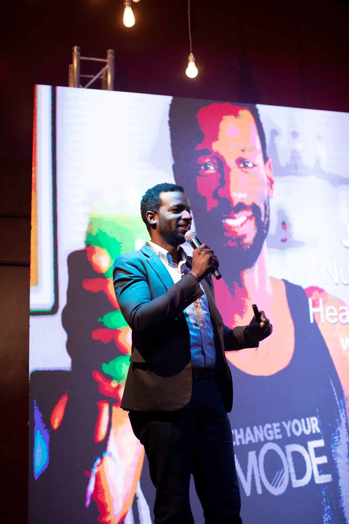 Justin Blyden speaking on stage, microphone in hand, in front of a screen reading Change Your Mode
